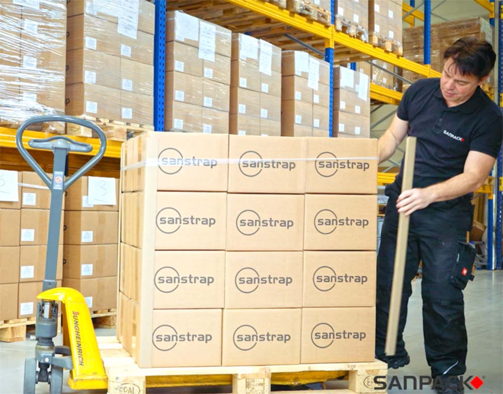 An employee secures a tall stack of cardboard boxes in the warehouse with sanstrap® stretch straps on a pallet.